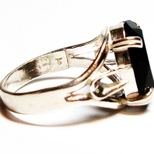 Puede incluir: Un anillo de plata con una piedra preciosa negra engastada en un dise&ntilde;o delicado y calado. El anillo tiene una banda simple y un engaste &uacute;nico que permite que la piedra preciosa destaque.