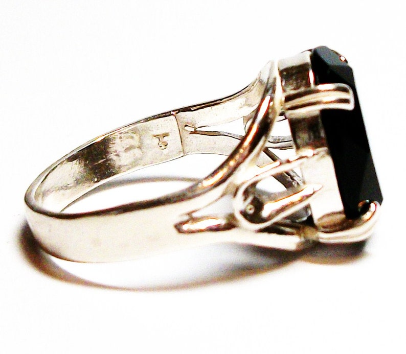 Puede incluir: Un anillo de plata con una piedra preciosa negra engastada en un dise&ntilde;o delicado y calado. El anillo tiene una banda simple y un engaste &uacute;nico que permite que la piedra preciosa destaque.