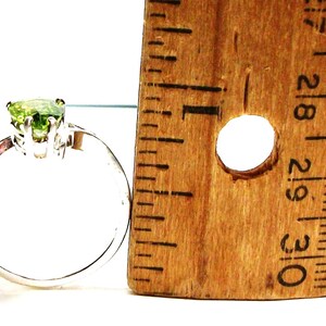 May include: A silver ring with a green gemstone in the centre. The ring is next to a ruler, showing the size of the stone.
