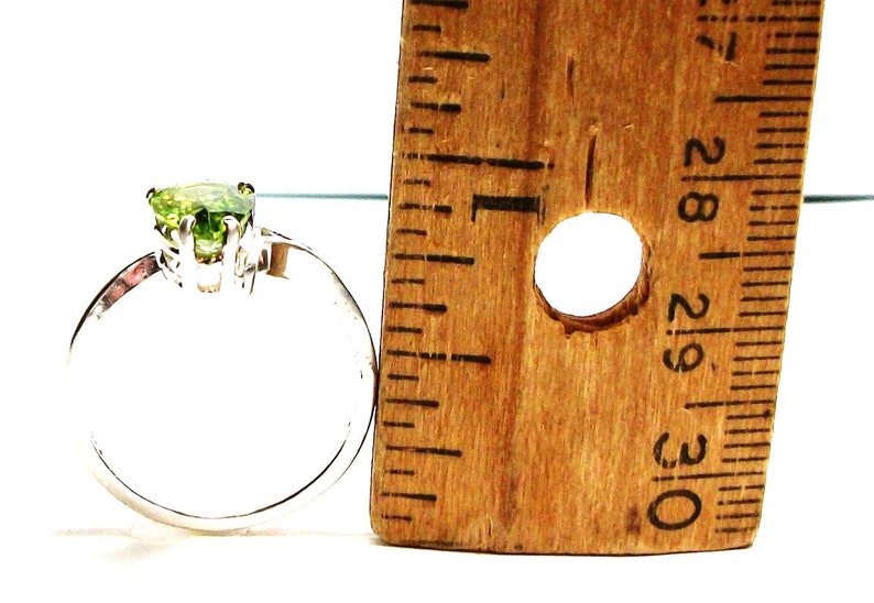 May include: A silver ring with a green gemstone in the centre. The ring is next to a ruler, showing the size of the stone.