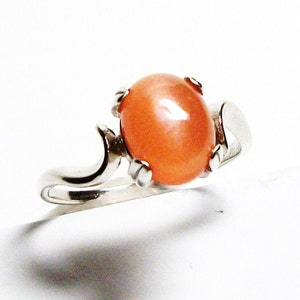 May include: A silver ring with a large, oval-shaped, peach-colored gemstone set in a prong setting.