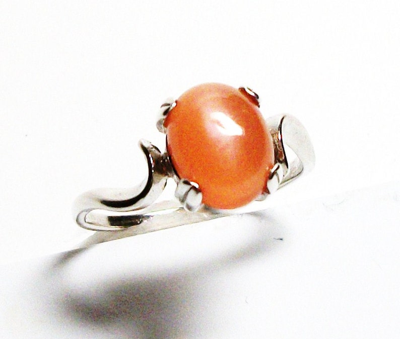May include: A silver ring with a large, oval-shaped, peach-colored gemstone set in a prong setting.