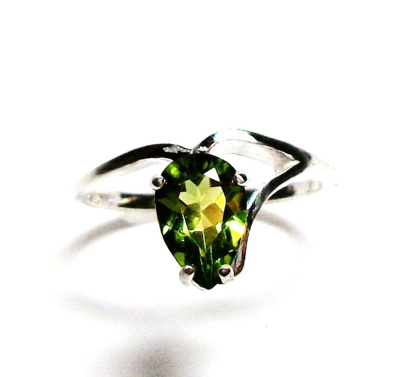 May include: A pear-shaped green gemstone ring set in a silver band with a twisted design.