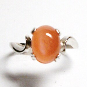 May include: A silver ring with a peach-colored oval gemstone set in a prong setting. The ring band is curved and has a smooth finish.