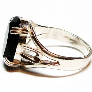 Puede incluir: Un anillo de plata con una gran piedra preciosa negra engastada en una banda decorativa de trabajo abierto.