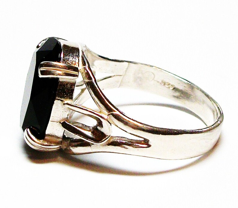 Puede incluir: Un anillo de plata con una gran piedra preciosa negra engastada en una banda decorativa de trabajo abierto.