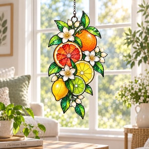 May include: A stained glass suncatcher featuring a cluster of citrus fruits including a whole orange, a sliced grapefruit, a sliced lemon, a whole lemon, and a sliced lime, accented with white blossoms and green leaves, suspended by a metal chain.