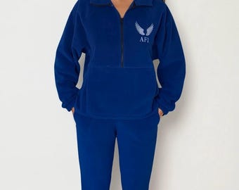 May include: A blue fleece tracksuit. The top has a half-zip closure and the text "AFI" with a wing design. The pants are a matching blue color. The outfit is made of a soft, warm material.
