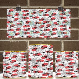 May include: A ceramic mug featuring a repeating pattern of red and black spider masks and small black spiders set against a white background with intricate black spider web lines. The design wraps around the exterior of the cylindrical mug.