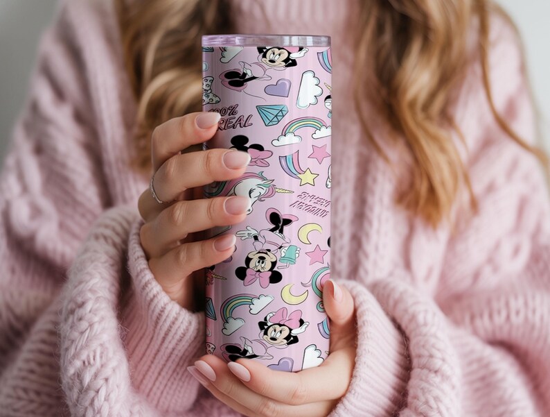 May include: A pink tumbler featuring a repeating pattern of cartoon characters, rainbows, stars, and the text "100% REAL". The tumbler is cylindrical and appears to be made of stainless steel. The design includes Minnie Mouse and other whimsical elements.