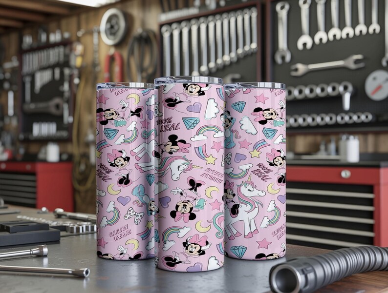 May include: Three pink insulated tumblers with a repeating pattern of Minnie Mouse, unicorns, rainbows, and diamonds. The text "100% REAL" and "UNICORN DREAM" are also featured. The tumblers are cylindrical and appear to be made of stainless steel.