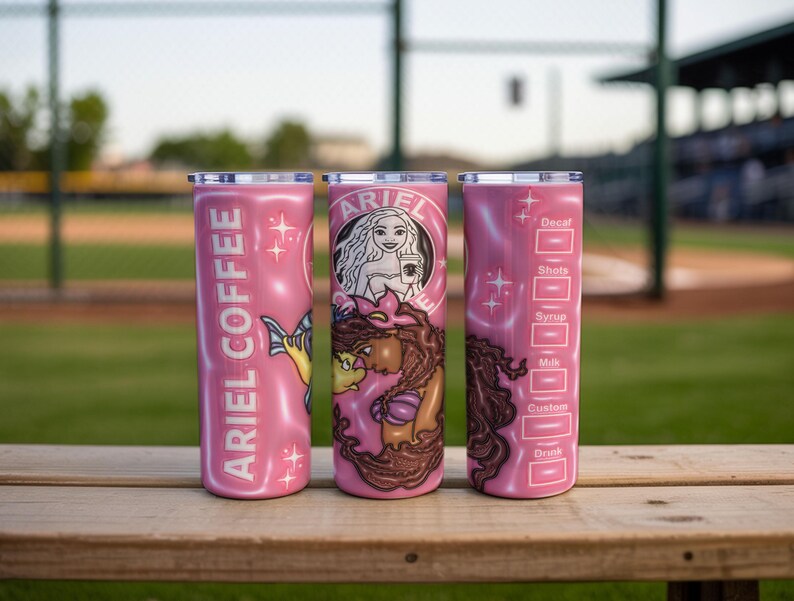May include: Three pink insulated tumblers with silver lids. One tumbler has "ARIEL COFFEE" in white text and a mermaid illustration. The second tumbler features a mermaid design with the text "ARIEL". The third tumbler has a coffee customization chart.