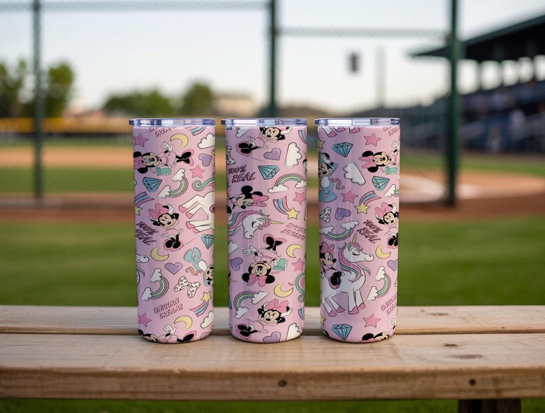 May include: Three pink insulated tumblers with a repeating pattern of Minnie Mouse, rainbows, stars, diamonds, and unicorns. The text "100% REAL" is also visible on the tumblers. The tumblers are cylindrical and have silver lids.