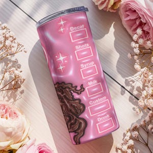 May include: A pink insulated travel mug with a coffee order chart design. The mug has sections for "Decaf," "Shots," "Syrup," "Milk," "Custom," and "Drink." Decorative elements include star shapes and a brown swirl design. Pink flowers surround the mug.