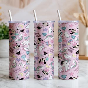 May include: Three pink insulated tumblers with white straws. The tumblers feature a repeating pattern of Minnie Mouse, unicorns, rainbows, diamonds, and the text "100% REAL" and "UNICORN DREAMS".