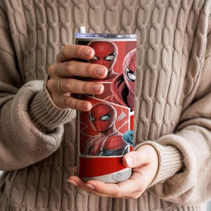 Pu&ograve; includere: Un bicchiere rosso e bianco con l'arte dei fumetti di Spider-Man. Il design include pi&ugrave; immagini del volto e della maschera di Spider-Man. Il bicchiere ha un coperchio argentato e una cannuccia bianca.