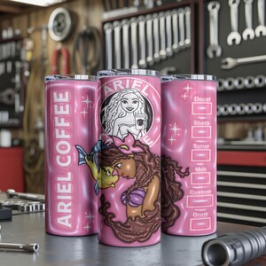 May include: Three pink insulated tumblers with a mermaid theme. One has "ARIEL COFFEE" vertically. Another features a mermaid graphic with the Starbucks logo. The third has a coffee customization chart. The tumblers are on a metal surface.