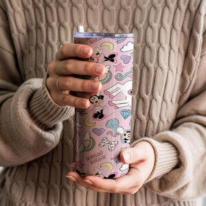 May include: A pink tumbler with a whimsical pattern featuring a unicorn, Mickey Mouse, rainbows, and hearts. The tumbler has a straw and the words "Unicorn Dreams" are printed on the side. The design is in pastel colors.