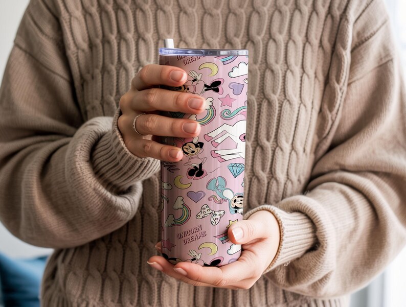 May include: A pink tumbler with a whimsical pattern featuring a unicorn, Mickey Mouse, rainbows, and hearts. The tumbler has a straw and the words "Unicorn Dreams" are printed on the side. The design is in pastel colors.