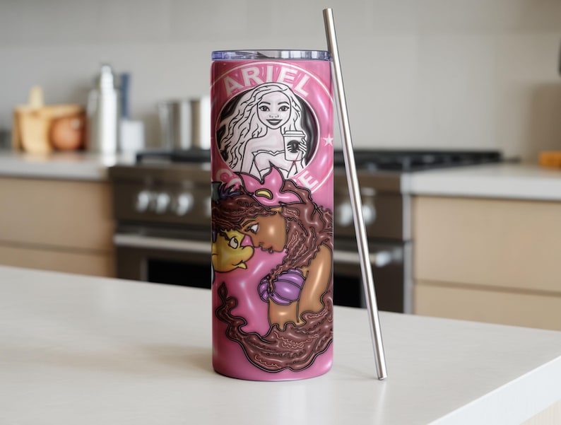 May include: A pink tumbler with a stainless steel straw. The tumbler features a cartoon illustration of Ariel from The Little Mermaid, with the name "ARIEL" in a circular design at the top. The design includes Ariel holding a coffee cup.