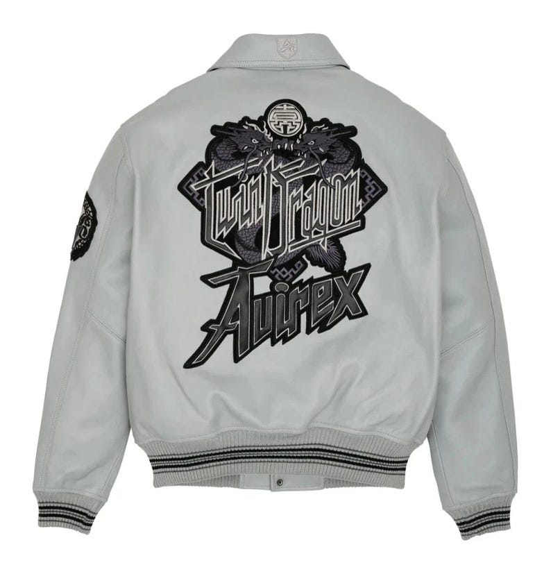 May include: Light gray bomber jacket with a black and gray "Twin Dragon" graphic on the back. The jacket features a collared neckline, ribbed cuffs, and the "Avirex" logo. A small patch is on the left sleeve.