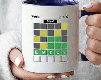 May include: White ceramic mug with a blue interior and handle, featuring a Wordle game design. The game shows the word "EMILY" correctly guessed. The word "Great" is displayed above the game board.