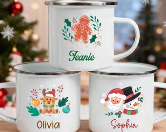 May include: Three white enamel mugs with silver rims, each featuring a different Christmas design. One mug has a gingerbread man, another a reindeer, and the third a Santa and snowman. Names are printed on each mug.