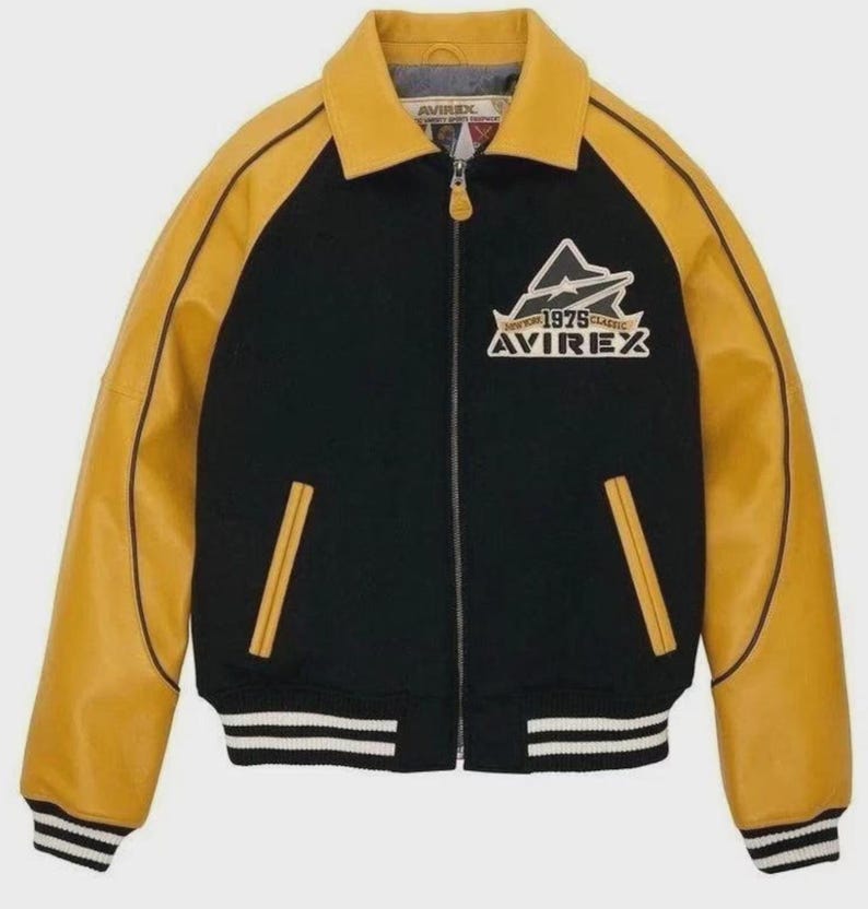 Puede incluir: Chaqueta bomber negra y amarilla con cremallera. La chaqueta presenta mangas y cuello de cuero amarillo, con un cuerpo negro. La parte delantera muestra un logotipo blanco y amarillo con el texto "BOSTON 1979 CLASSIC AVIREX". La chaqueta tiene dobladillo y pu&ntilde;os acanalados.