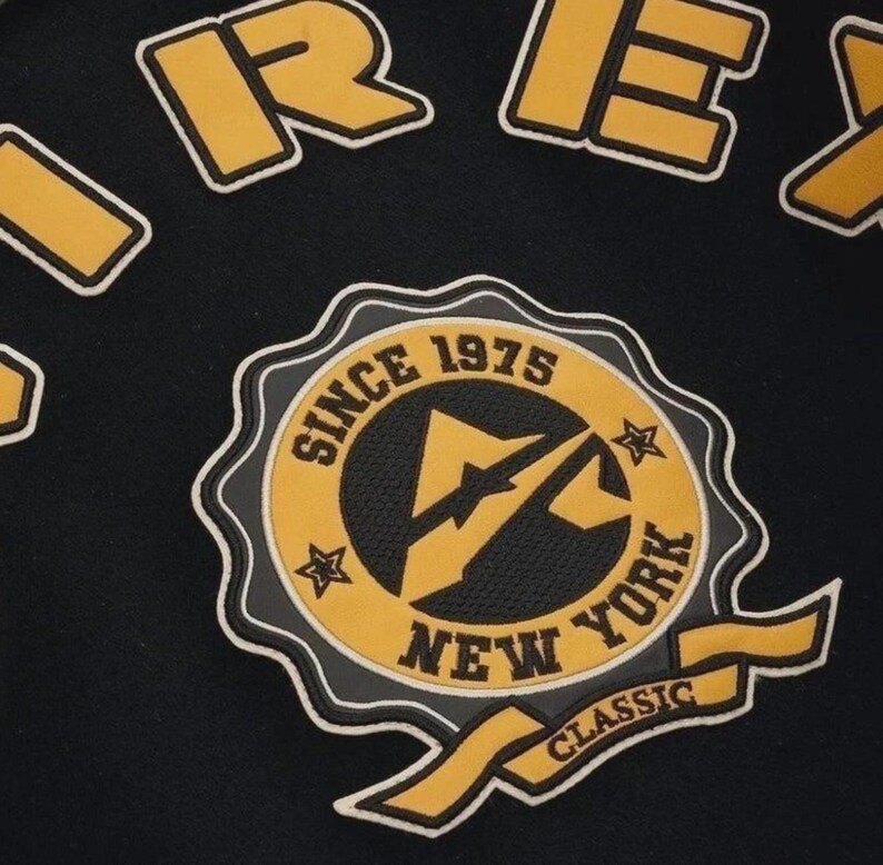 Puede incluir: Tela negra con un parche bordado amarillo y blanco. El parche dice "SINCE 1975 NEW YORK CLASSIC" alrededor de un logotipo central. Se ve texto amarillo y blanco adicional en la parte superior.