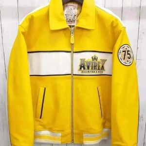Puede incluir: Chaqueta de cuero amarilla con una franja blanca en el pecho y las mangas. Presenta el logotipo "AVIREX AVIATOR'S KING" y un parche "75". Incluye cierre de cremallera y cuello.
