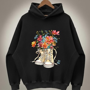 May include: Black hoodie featuring a floral design. The graphic shows a pair of cream-colored high-top sneakers filled with a bouquet of colorful flowers. The flowers include pink, orange, blue, and yellow blooms.