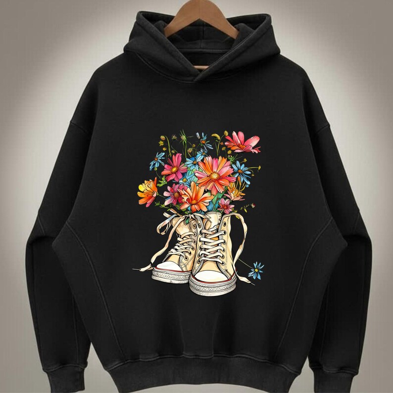 May include: Black hoodie featuring a floral design. The graphic shows a pair of cream-colored high-top sneakers filled with a bouquet of colorful flowers. The flowers include pink, orange, blue, and yellow blooms.