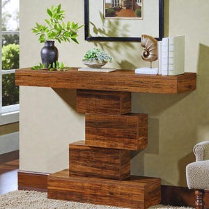 Peut inclure: Une console moderne en bois foncé avec un design unique en blocs empilés. La table présente un long plateau flottant avec une série de blocs rectangulaires formant la base. Le grain du bois est visible, contre un mur neutre.