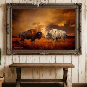 May include: A framed wall art print featuring a dark brown bison and a white bison standing in a golden grassy field under a dramatic sunset sky. The ornate dark frame surrounds the landscape scene, which includes the signature Cassidy A. Caputo.