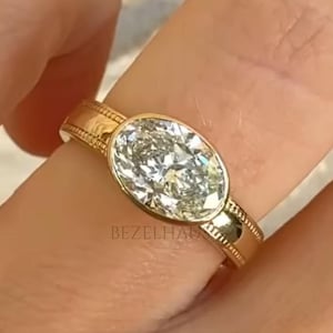 Op de afbeelding: Een gouden ring met een ovale, heldere edelsteen. De ring heeft een getextureerde band en wordt om een vinger gedragen. De ring is een sieraad.