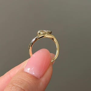 Puede incluir: Un anillo de oro con una gema grande y transparente. El anillo tiene un dise&ntilde;o simple y elegante con una banda lisa y pulida. La gema est&aacute; engastada en un engaste de bisel.