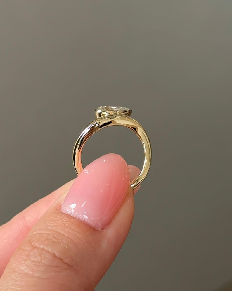 Puede incluir: Un anillo de oro con una gema grande y transparente. El anillo tiene un dise&ntilde;o simple y elegante con una banda lisa y pulida. La gema est&aacute; engastada en un engaste de bisel.