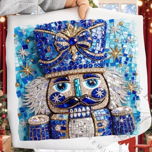 May include: A decorative pillow featuring a detailed mosaic design of a nutcracker soldier. The nutcracker is predominantly blue with gold accents, sparkling embellishments, and a large bow. The pillow is held against a festive holiday backdrop.
