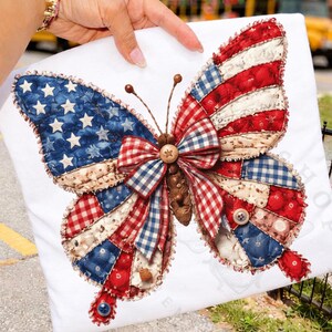 Puede incluir: Un cojín cuadrado blanco con un diseño de mariposa. Las alas están hechas de tela de retazos roja, blanca y azul. El cuerpo de la mariposa es marrón y las antenas son alambres marrones finos. El cojín tiene un tema patriótico.