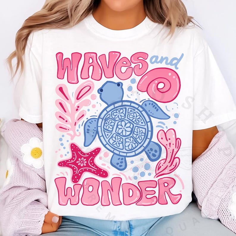 Pu&ograve; includere: T-shirt bianca con un design grafico colorato raffigurante una tartaruga blu, una stella marina rosa e le parole "Waves and Wonder" in rosa. Il design include elementi a tema marino come una conchiglia e coralli.
