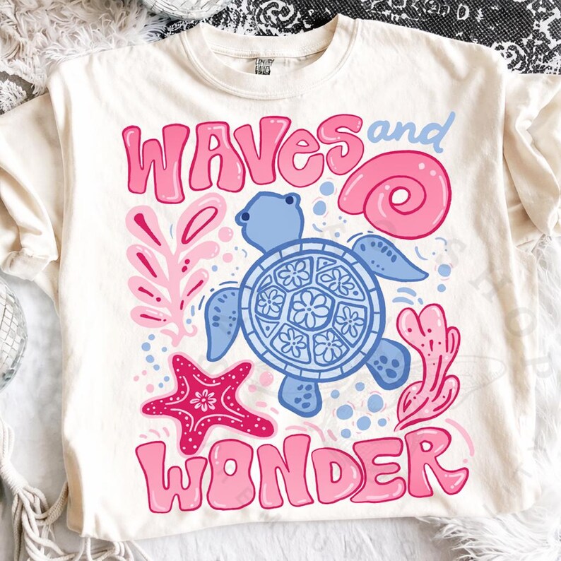 Pu&ograve; includere: T-shirt color crema con un design stravagante. Le parole "WAVES and WONDER" sono in rosa e blu. Il design include una tartaruga blu, una conchiglia rosa, una stella marina rosa e coralli rosa.