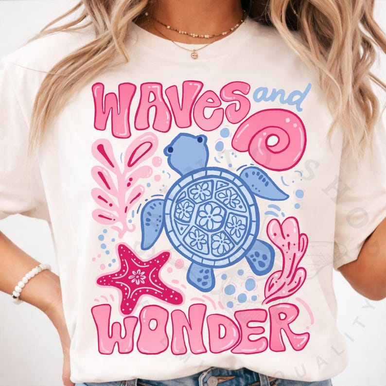 Pu&ograve; includere: T-shirt color crema con grafica a tema oceano. Il design include una tartaruga blu, una stella marina rosa e le parole "WAVES and WONDER" in rosa e blu. La maglietta ha maniche corte.