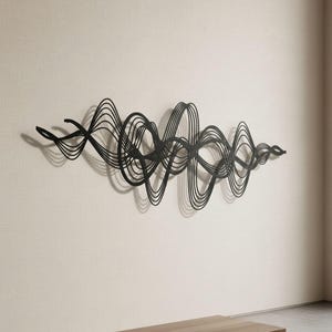Könnte beinhalten: Schwarze Metall-Wandkunst, die ein abstraktes Wellenmuster darstellt. Das Kunstwerk ist an einer hellen Wand befestigt und wirft Schatten. Eine Holzbank ist im Vordergrund zu sehen, was der Szene Tiefe verleiht. Dieses moderne Stück eignet sich für die Inneneinrichtung.