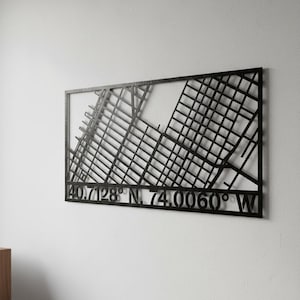 May include: Black metal wall art depicting a city map with street grid details. The artwork includes the coordinates 40.7128° N, 74.0060° W. The piece is rectangular and mounted on a white wall.