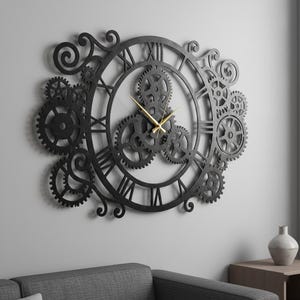 May include: A large, black, steampunk-style wall clock with Roman numerals and decorative gears. The clock hands are gold. The clock is mounted on a light gray wall, with a gray sofa and wooden table in the foreground.