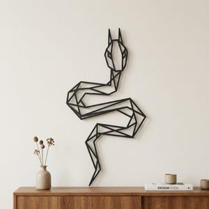 May include: A black metal wall art piece shaped like a stylised snake with a geometric, angular design. The snake is depicted in a vertical, winding position with a pointed head and two upright ears, featuring a series of interconnected lines.
