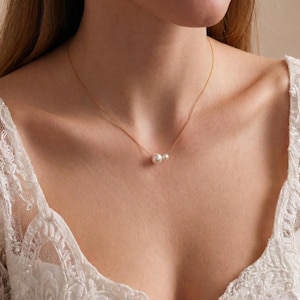 May include: A delicate gold necklace featuring three white pearls. The necklace is worn on a person wearing a white lace top. The gold chain is thin and the pearls are evenly spaced, creating a simple yet elegant design.