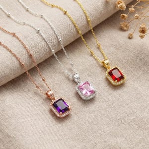 Puede incluir: Cuatro collares con colgantes de piedras preciosas. Los colgantes son rectangulares y presentan piedras de amatista, rosa y roja. Las cadenas son de oro, plata y oro rosa. Cada colgante está rodeado de pequeñas piedras transparentes.