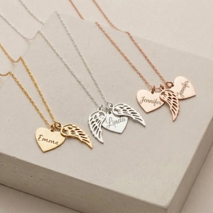 May include: A collection of personalized heart-shaped pendant necklaces in gold, silver, and rose gold. Each necklace features a heart pendant with a name engraved and a wing charm. The names "Emma", "Linda", and "Jennifer" are visible.