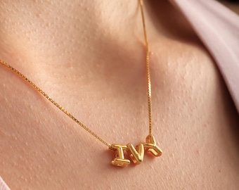 May include: A gold-colored necklace with the letters "IVY" as a pendant. The necklace is worn around the neck and is made of a delicate chain. The letters are in a bold, rounded font.